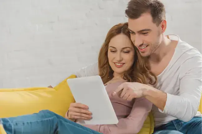 jeune couple heureux utilisant une tablette numérique tout en étant assis sur un canapé à la maison