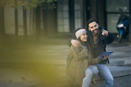 Un jeune couple heureux explore une ville et montre du doigt au loin.