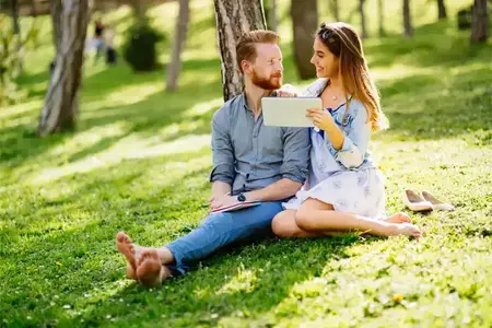 Un jeune couple affectueux partage une tablette dans un parc urbain