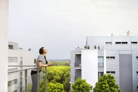 Femme avec une tasse de café debout sur le balcon d'un logement neuf