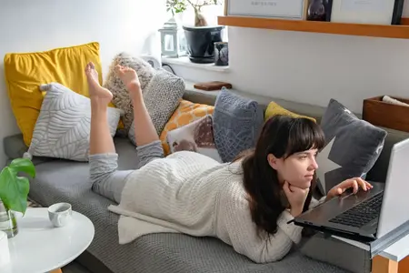 Jeune femme se relaxant sur le canapé et utilisant un ordinateur portable