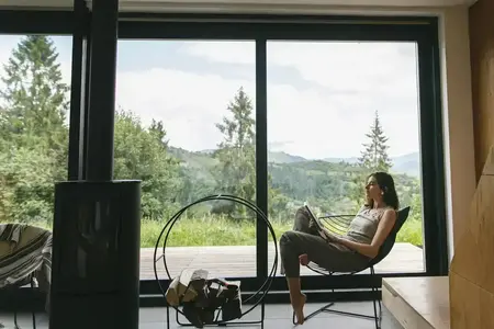 Belle femme élégante lisant un livre, assise sur une chaise devant la cheminée sur fond de collines de montagne