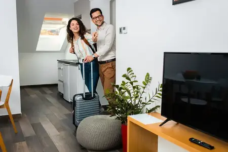 Couple souriant avec valise arrivant dans la chambre airbnb