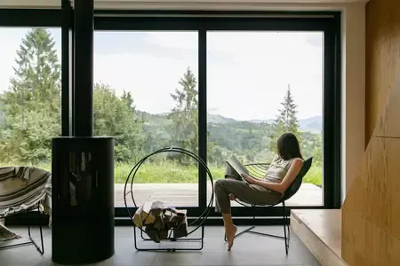 Belle femme élégante lisant un livre, assise sur une chaise devant la cheminée sur fond de collines de montagne
